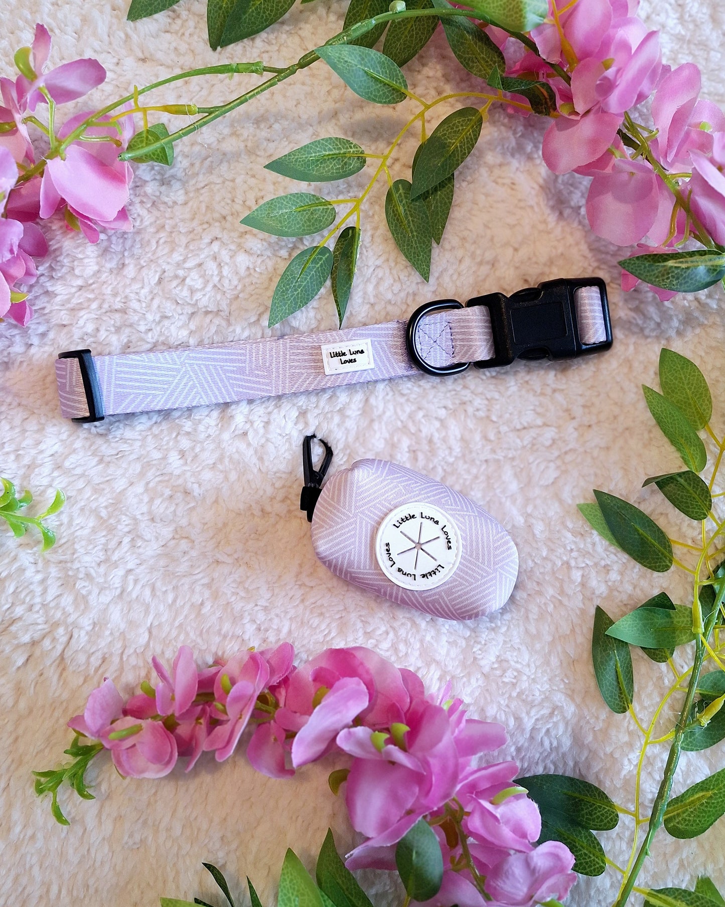 Adjustable dog collar in lavender color with a quick release buckle and a durable D ring, presented on a soft texture with floral accents.