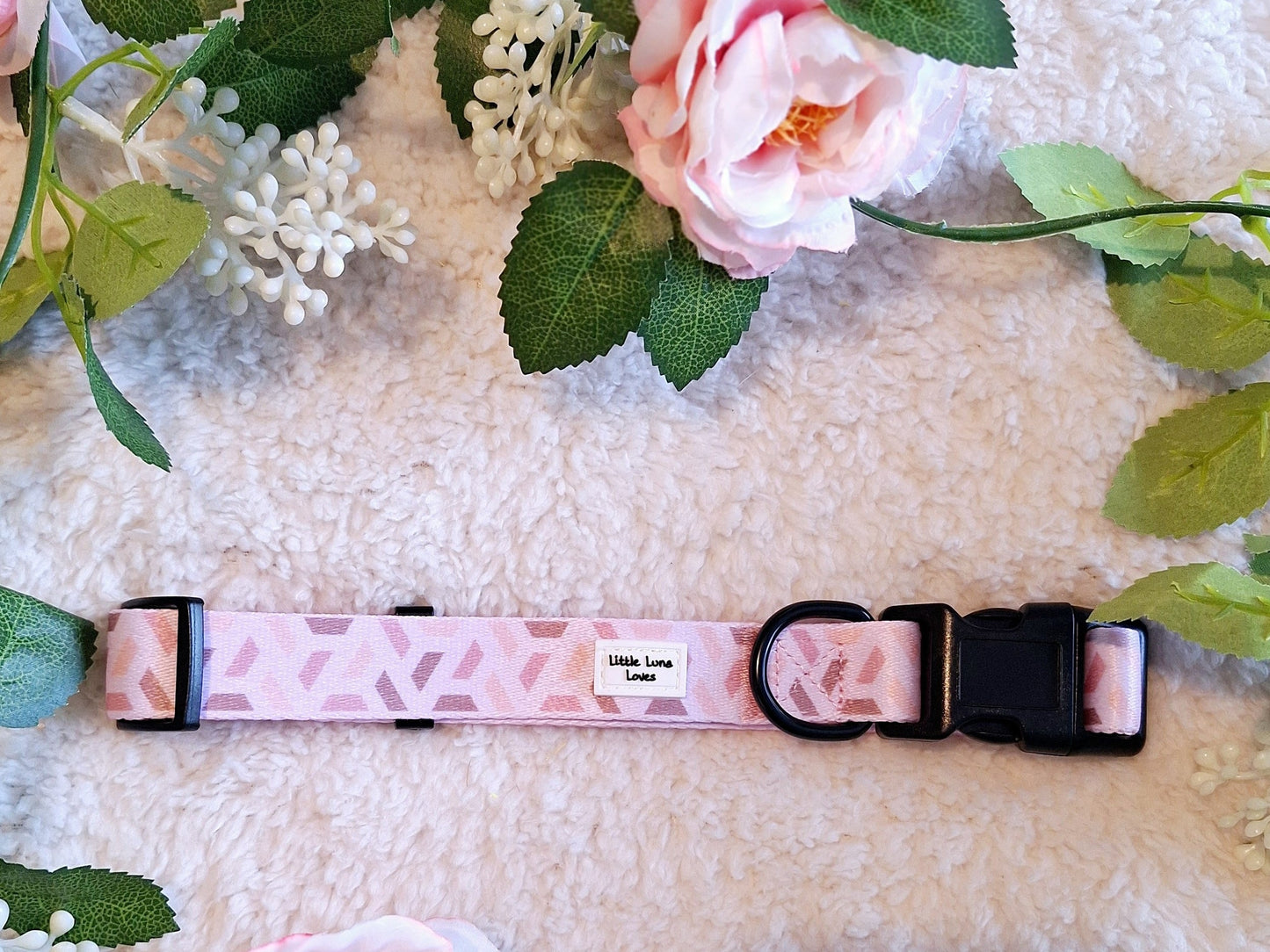 Adjustable pink dog collar with a black quick release buckle and D ring, displayed on a white faux fur surface with flowers in the background.