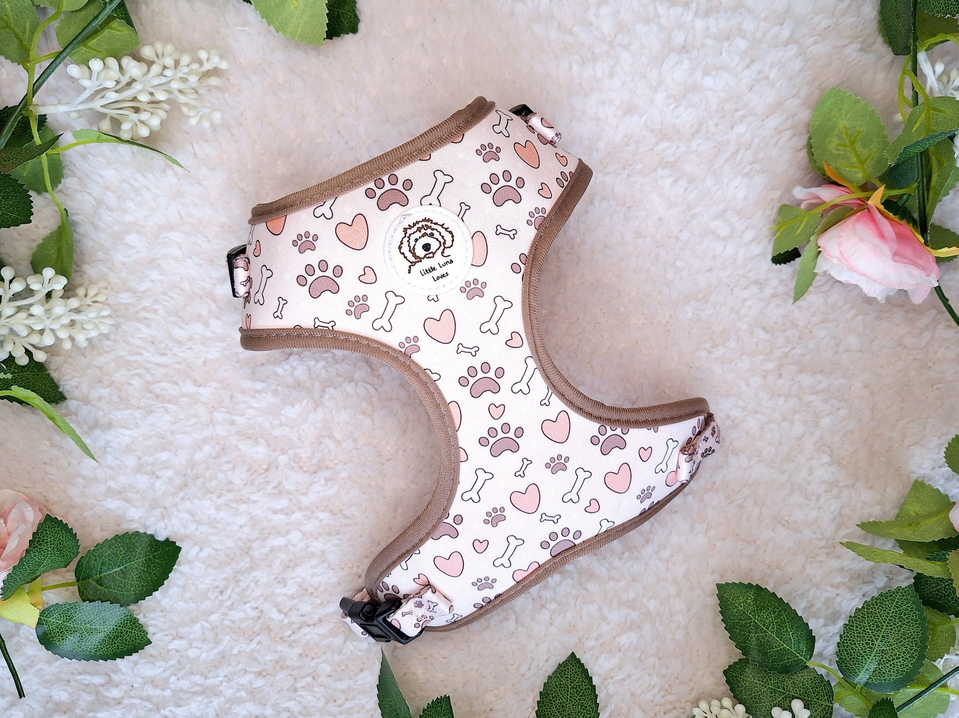 adjustable dog harness with bone, paws and hearts, laid out with flowers around it