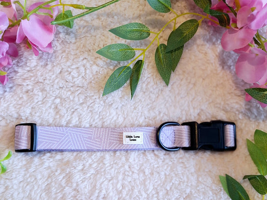 Adjustable dog collar in lavender and white colors with a quick release buckle and a D-ring, displayed on a fluffy surface with pink flowers around.