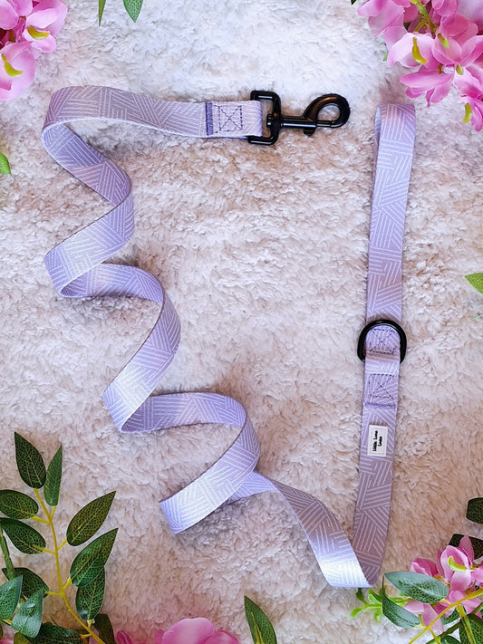 A lavender-colored dog lead laid out on a soft surface with a swivel back clip and D ring visible, surrounded by decorative flowers.