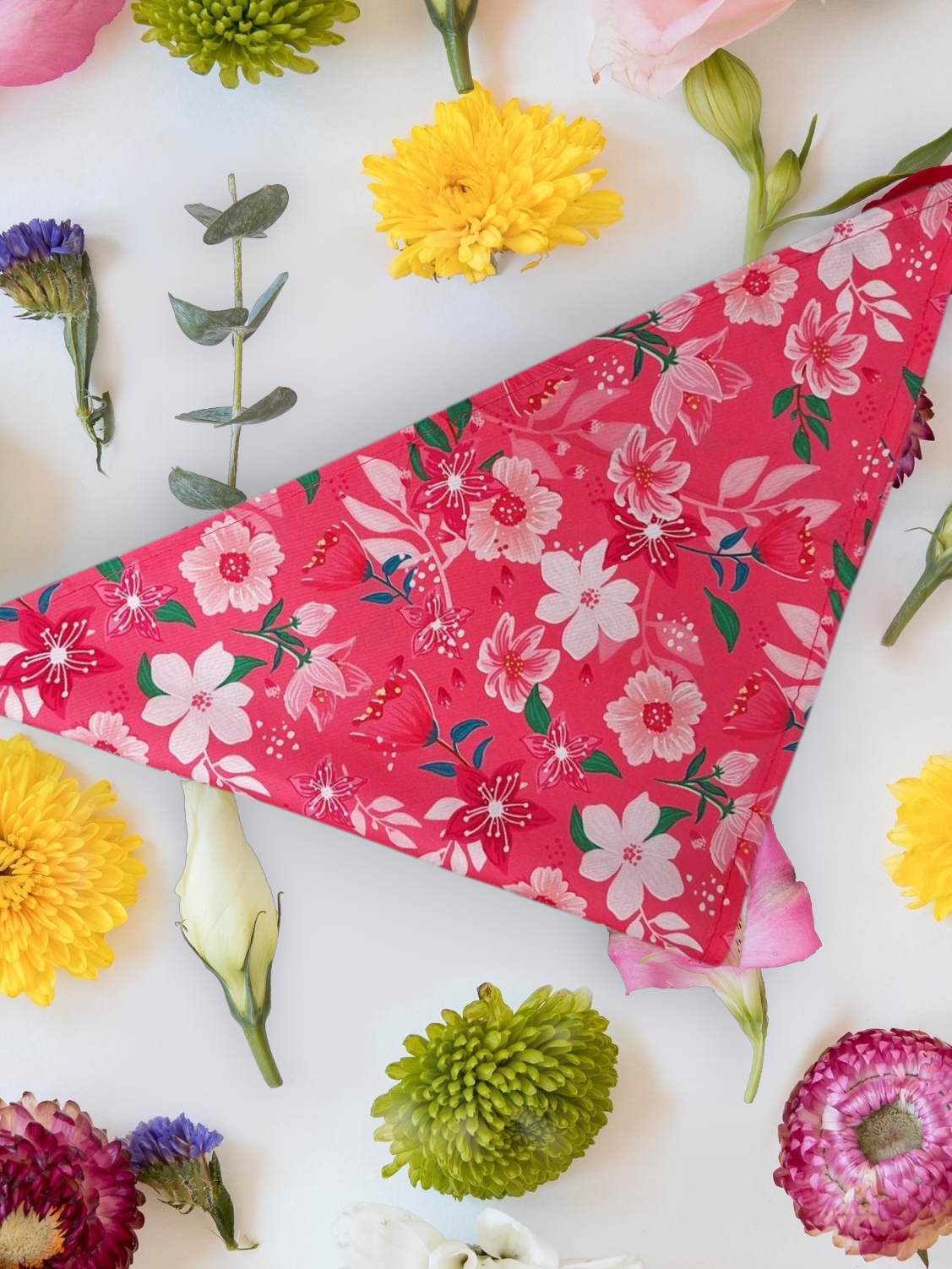 pink dog bandana with floral design laid out with flowers around it