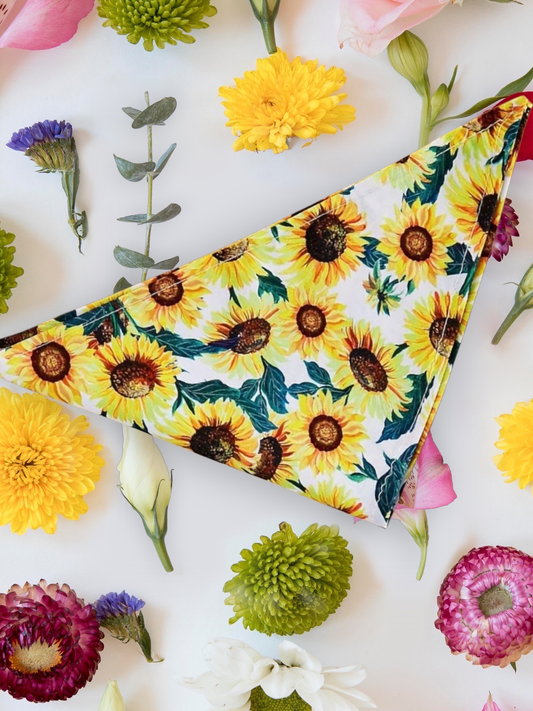 A floral sunflower patterned neck tie bandana laid out flat with various colorful flowers around it.