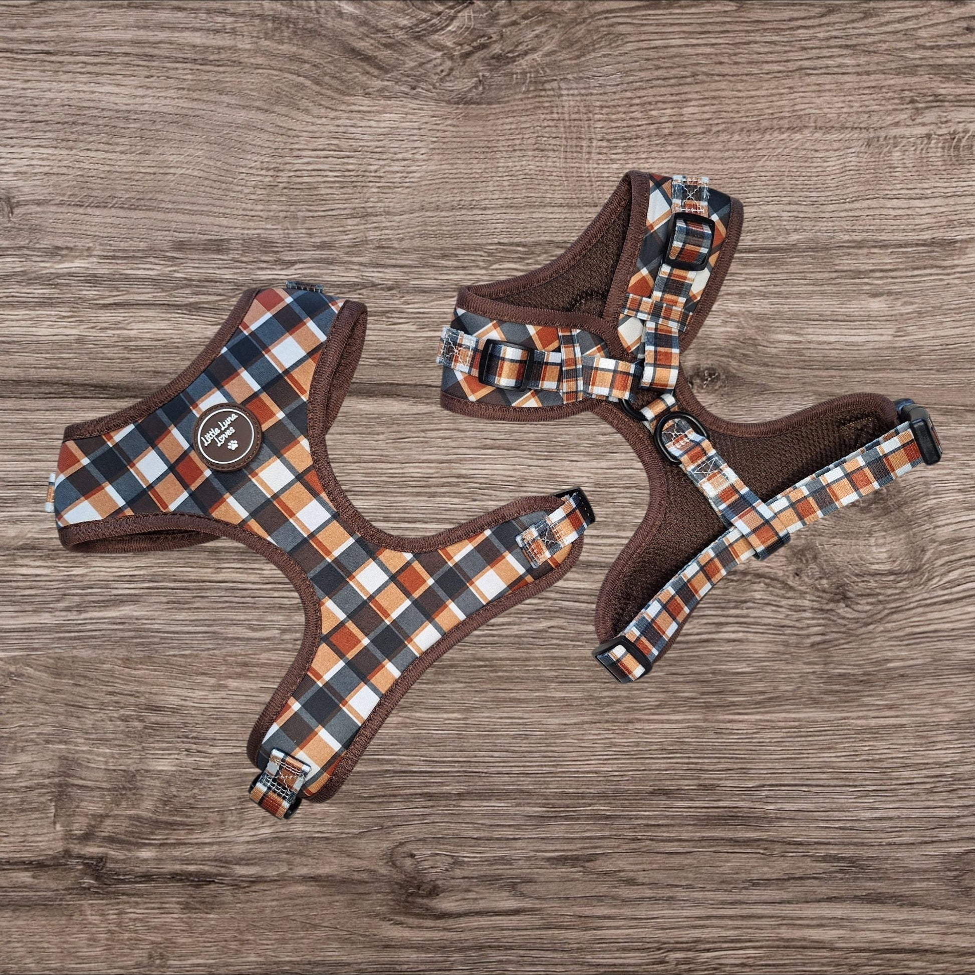 Two dog harnesses with a brown, orange, and white plaid pattern and solid brown mesh lining, displayed on a rustic wood background.
